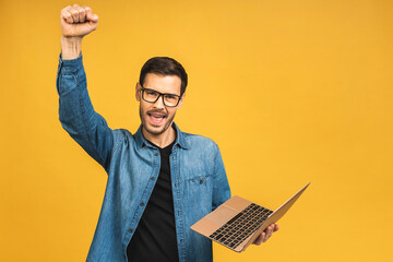 Image of happy excited young man posing isolated over yellow background wall using laptop computer...