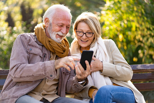 Cheerful elderly couple using banking apps on a smartphone to make payments outdoors in the park