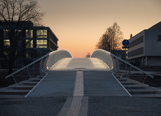 A new footbridge in a modern style in Hradec Králové. An administrative building in the background. View of sunrise.