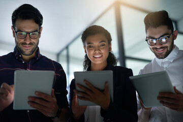 Engaging technology as a team. Shot of three colleagues using digital tablets while standing together in an office.