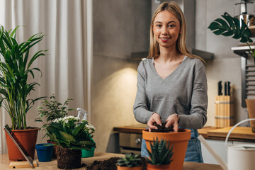 Young caucasian woman is placing soil in a flowerpot