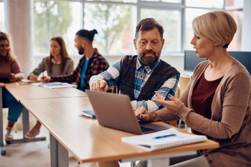 Mature and and his female classmate e-learning on laptop in classroom.