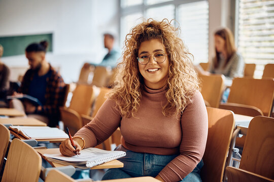 Happy female college student learning at lecture hall and looking at camera.