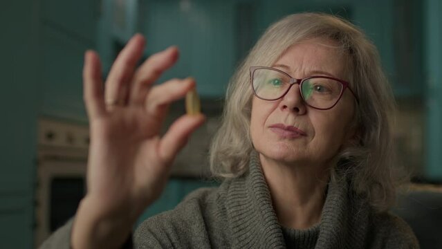 Senior Woman Holding Capsule In Hand. 60s woman taking care of health. Omega-3 fish oil for elderly people is very healthy.