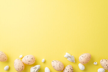 Easter decorations concept. Top view photo of easter quail eggs and ceramic bunnies on isolated yellow background with copyspace