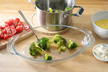 Blanched broccoli is filled into a glass baking dish, cooking preparation for a casserole with...