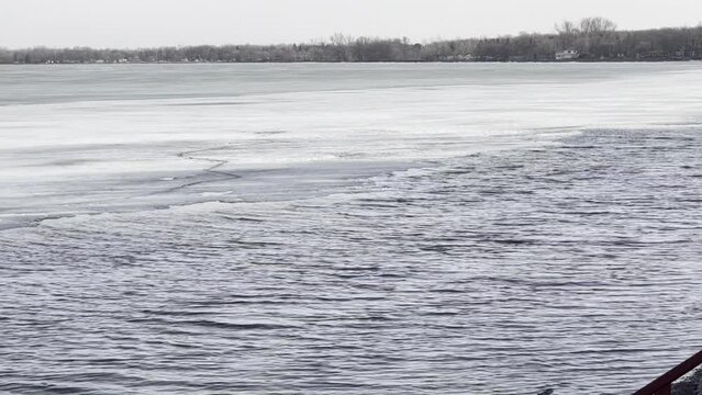 A frozen lake begins to melt, revealing open water near shore