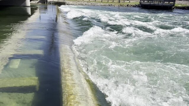 Clear river flowing over concrete dam creates waves and foam