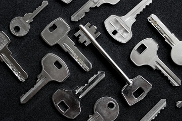A pattern of different types of keys from locks laid out on black surface top view
