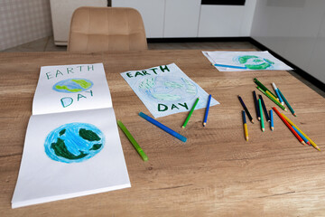 Children's drawings of the planet Earth with a world map with multi-colored pencils on white paper lie on the kitchen table at home. The concept of the day of peace and earth