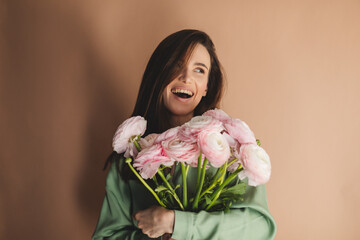 International Women's Day. Extremely happy woman in green shirt enjoying a bunch of spring flowers ranunculus, which she is holding in her hands. Happy girl laughing and look at side.