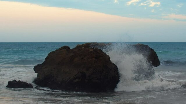 Slow motion video of waves crashing against a large boulder in the coastal zone