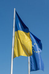 Ukrainian and European flag waving at a flagpole with blue sky in background and copy space