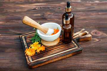 glass bottle essential oil of calendula and fresh calendula flowers leave on a cutting vintage...