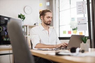 Fototapeta na wymiar Portrait of attractive young business man sitting at office desk and working with laptop. Caucasian guy with beard having video conference. Business meeting online.