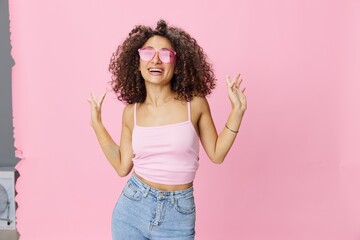 Happy woman afro curls hair dancing on a pink background in summer pink t-shirt jeans and glasses, summer vibe, copy space