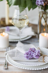 Obraz na płótnie Canvas Beautiful table decor for a wedding dinner with a spring blooming lilac flowers. Celebration of a special event. Fancy white plates, wineglasses, candles. Countryside style