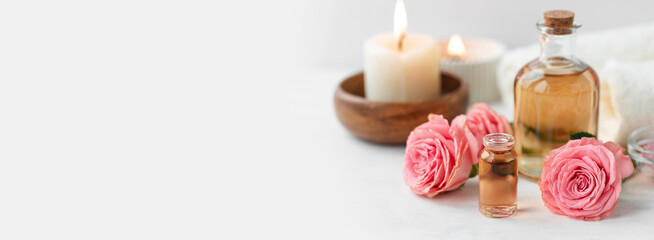Aromatherapy. Pure organic essential rose oil concept. Elixir with plant based floral herbal ingredients. Pink flowers extract. Spa atmosphere with candle, towel. White background. Banner copy space