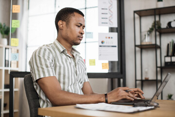 Fototapeta na wymiar Portrait of attractive young businessman sitting at office desk and working with laptop. African american guy having online video conference. Business meeting online.