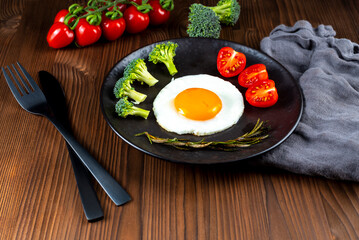 Fried soft-boiled egg on a black plate with fresh broccoli vegetables and tomatoes
