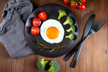 Fried soft-boiled egg on a black plate with fresh broccoli vegetables and tomatoes