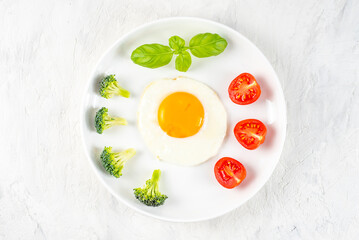 Fried soft-boiled egg on a white plate with fresh broccoli vegetables and tomatoes