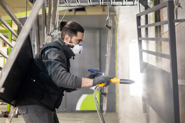 A man working in a factory finishes a job using the electrostatic powder coating technique with a...