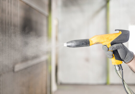 Detail of the hand of a man working in a factory finishing a job using the electrostatic powder coating technique with a spray gun. Metal factory works concept.