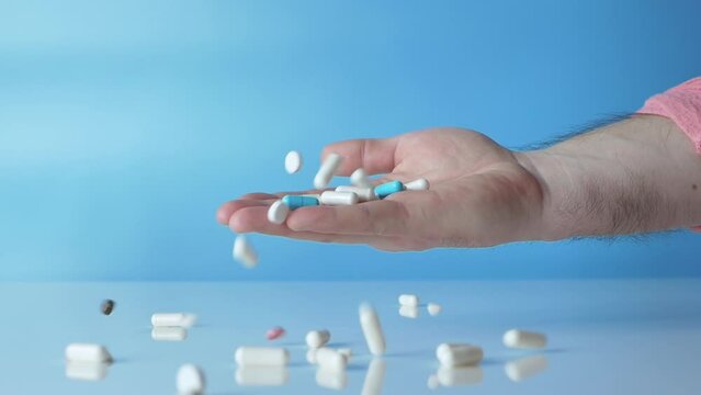 Human health concept. Falling pills in a person's hand in slow motion on a blue background. Medical capsules, antistress tablets. Pharmaceutics. Antibiotic tablets.