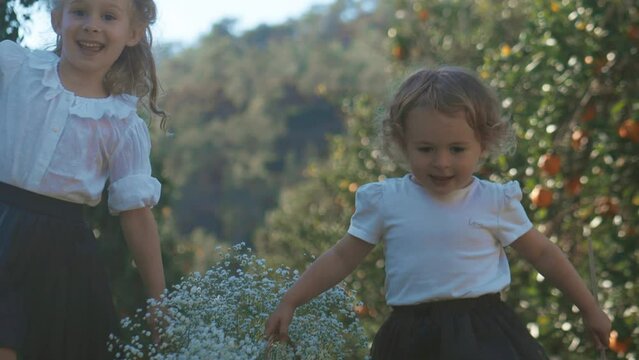 Little girls carry white flowers in basket in the garden together