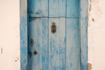 Old wooden door of colonial period house with peeling blue paint and rusty metal knocker and keyhole.