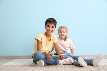 Little boy and girl watching cartoons on tablet computer near blue wall