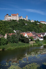 Fototapeta na wymiar Landscape shot of Harburg Castle in Bavaria, which stands on the bank of a river. The castle stands on a hill above a village. In between is a forest. The blue sky above.