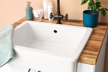 Fototapeta na wymiar Table with sink, bath accessories and houseplant near beige wall, closeup