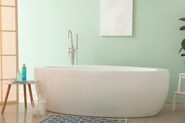 Fototapeta na wymiar Interior of bathroom with modern bathtub and bath accessories near green wall