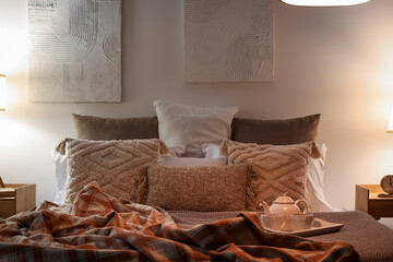 Tray with teapot and cups on bed in dark bedroom