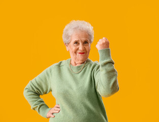 Happy senior woman in green sweater on yellow background