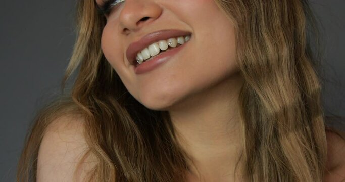 Beautiful young well-groomed woman with professional makeup smiles at camera, showing decorative jewelry on her teeth
