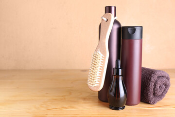 Bottles of cosmetic products, massage brush and towel on wooden table against color background