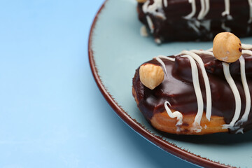 Plate with delicious chocolate eclairs on blue background