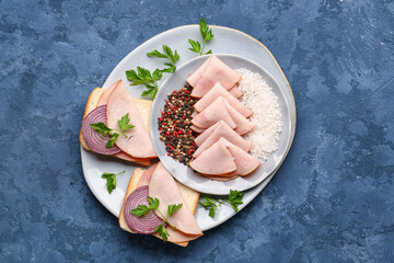 Plate with slices of tasty ham, spices, parsley and bread pieces on blue grunge background