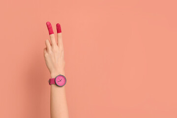 Woman with painted fingers and stylish wristwatch showing victory gesture on pink background