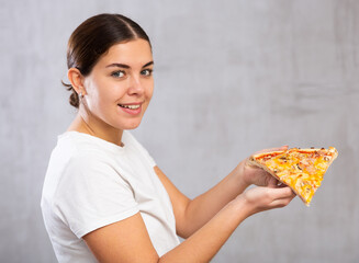 Photo of smiling young woman holding piece of pizza against gray shadeless background