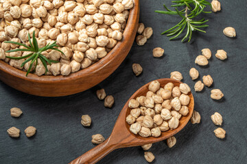 Dried raw chickpeas in wooden spoon and in wooden bowl, on a black background, closeup. Organic food. Legumes. Top view food. 