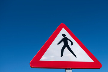 Dangerous pedestrian crossing traffic sign over a blue sky