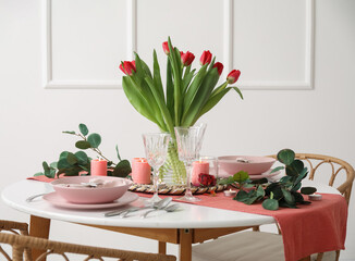 Table setting for International Women's Day celebration with tulip flowers, burning candles and eucalyptus branches in light room