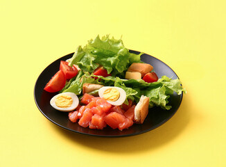 Plate of delicious salad with boiled eggs and salmon on yellow background