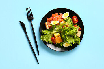 Plate of delicious salad with boiled eggs and salmon on blue background