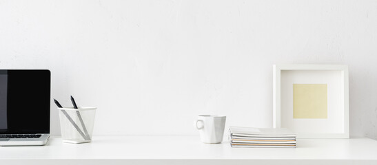 Desk with white office supplies, mug, frame, laptop and empty space. Mockup.