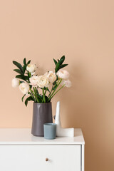 Vase with ranunculus flowers and decor on chest of drawers near beige wall